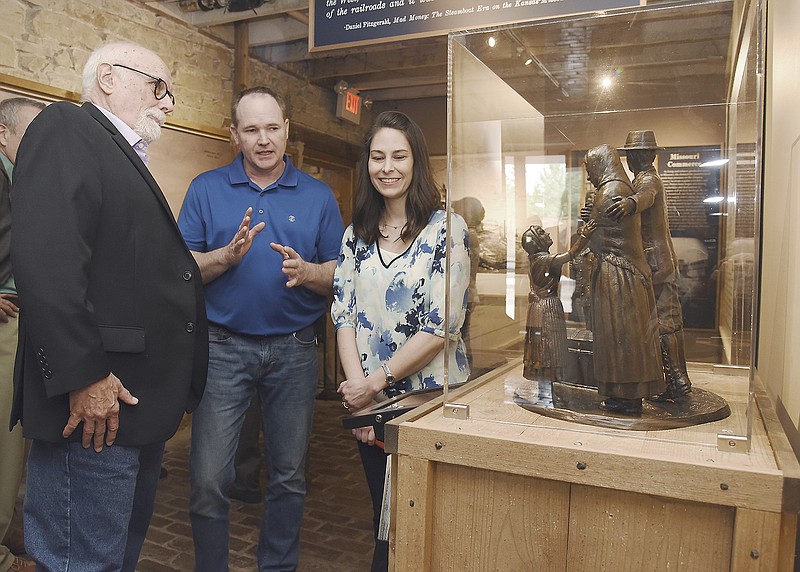 Sculptor William J. Williams, left, visits with Scott and Tisha Spencer with Firehouse Designs in Jefferson City who worked on the project and created the display cabinet for the statue. They visited after the "Immigrants Arriving" memorial statue, at right, was unveiled during a ceremony Monday at the Jefferson Landing State Historic Site.