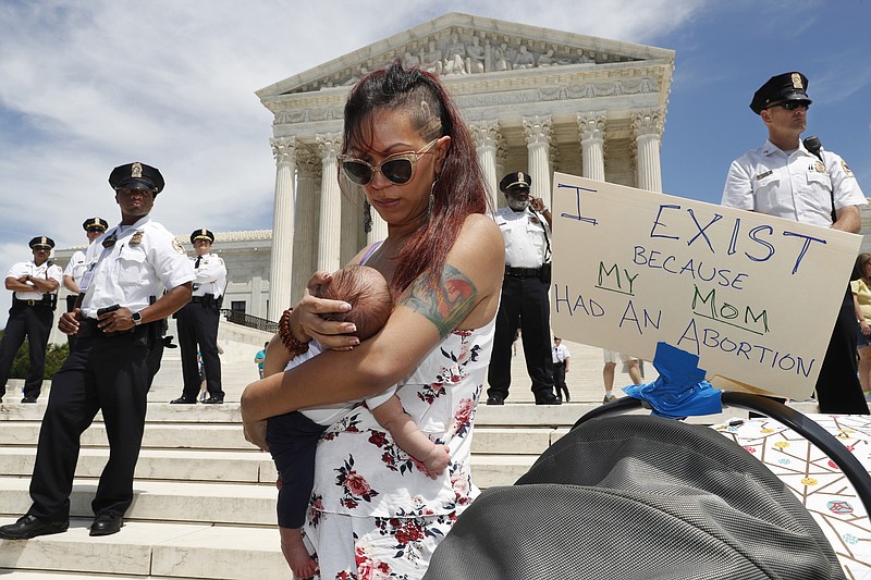 As security guards the steps of the Supreme Court, Kristin Mink of Silver Spring, Md., holds her three-week-old daughter by a sign she brought that says, "I exist because my Mom had an abortion," as Mink joined a protest against abortion bans, Tuesday, May 21, 2019, outside the Supreme Court in Washington. Being able to access abortion services in an earlier pregnancy made it possible for Mink to now give birth to this child. (AP Photo/Jacquelyn Martin)