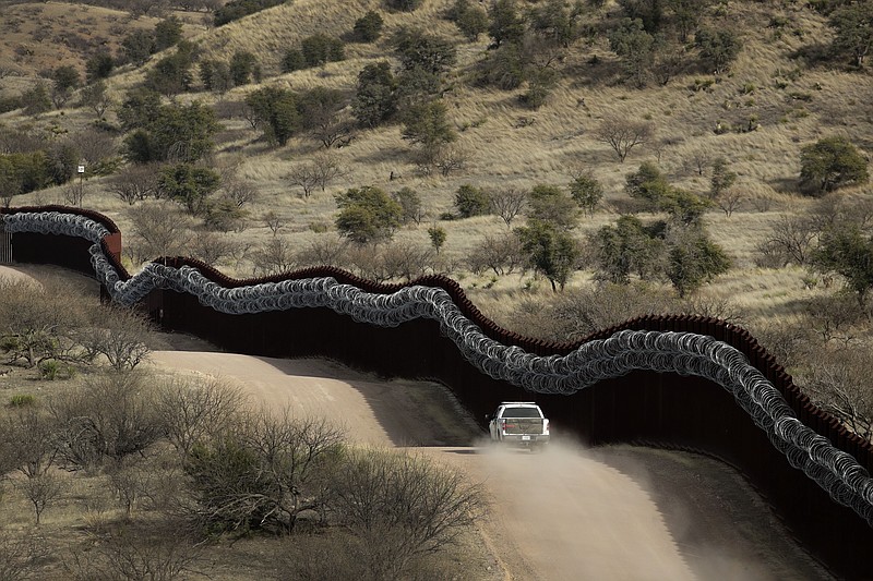 FILE - This March 2, 2019 photo shows a Customs and Border Control agent patrols on the US side of a razor-wire-covered border wall along the Mexico east of Nogales, Ariz.  A surge of asylum-seeking families that has strained cities along the southern U.S. border for months is now being felt in cities far from Mexico. Immigrants are being housed in airplane hangars and rodeo fairgrounds, while local authorities are struggling to keep up with the influx.(AP Photo/Charlie Riedel)