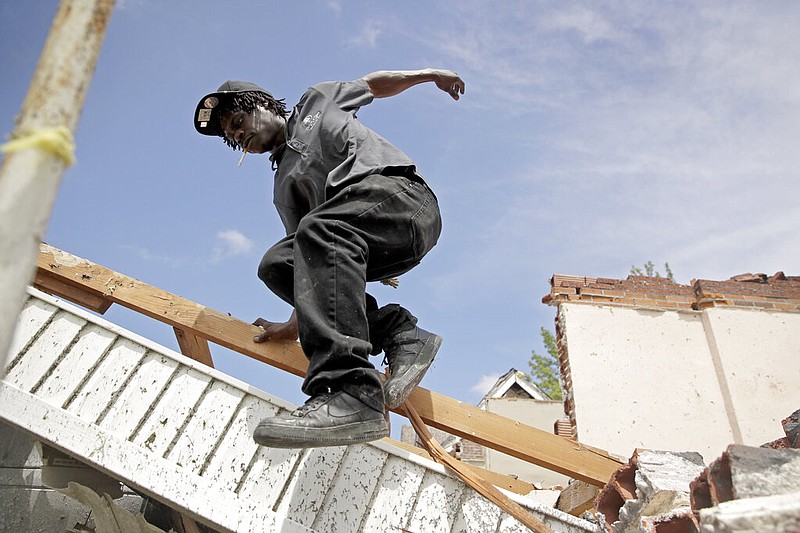 Tavaris McClain, left, jumps off a pile of debris as he cleans up outside his mother's destroyed home Thursday, May 23, 2019 after a tornado tore through Jefferson City late Wednesday. (AP Photo/Charlie Riedel)