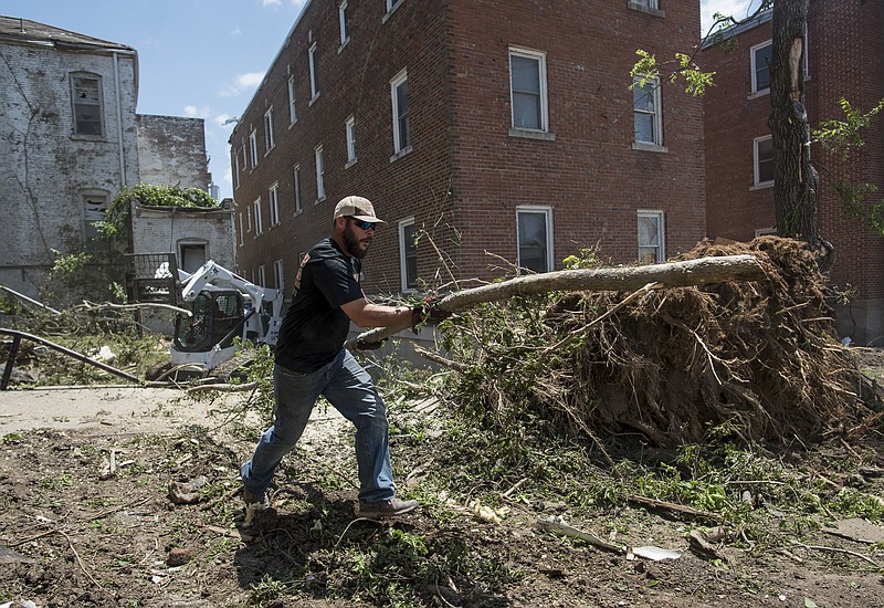 Kris Wilson/News Tribune
Gaines Landscaping & Lawn Care employee Hunter Thurman carries a tree limb to the Wilson Tree Service wood chipper as the two companies work together to clear a large tree that had fallen between four residential and office buildings in the 200 block of Marshall Street during tornado cleanup efforts in the historic Capitol Avenue district on Saturday afternoon. Gaines Landscaping & Lawn Care owner Sam Gaines operates the track lift in the background as he clears out some of the larger debris.