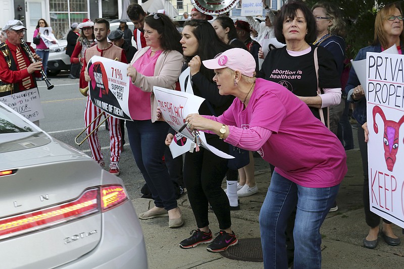 In this Thursday, May 23, 2019, photo, Nancy St Germain, 71, right, of Warwick, R.I., leans forward to show her sign to a driver leaving a fundraiser for the Rhode Island Senate Democrats political action committee in Providence, R.I. Her sign reads, "This fight isn't over." Protesters gathered at the fundraiser to pressure legislative leaders to bring a bill seeking to protect abortion rights to the Senate floor for a vote. (AP Photo/Jennifer McDermott)