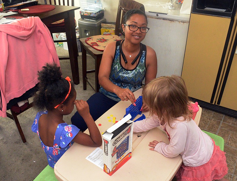 Mark Wilson/News Tribune
Lakaisha McCaleb plays a game with kids in her charge while talking about the challenges she faces getting her business back up and running Friday at her mother's house.