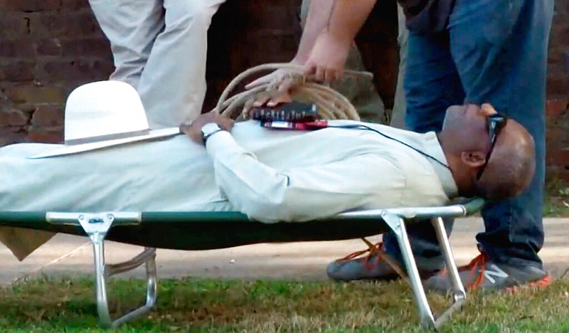 In this April 17, 2018 file image from video provided by KTHV-TV, a death penalty protester outside the Arkansas governor's mansion in Little Rock prepares to tie rope around Pulaski County Circuit Judge Wendell Griffen who is laying on a cot in protest of executions. An Arkansas disciplinary panel has dismissed an ethics case against Griffen, who faced the possibility of removal from the bench for participating in the anti-death penalty demonstration the same day he blocked the state from using an execution drug. Counsel for the Judicial Discipline and Disability Commission confirmed Wednesday, June 12, 2019, that the case against Griffen was dismissed because too much time had passed before the commission took up the case. (KTHV/TEGNA Inc. via AP, File)