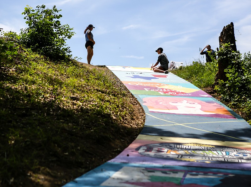 People walk by an artists working on their canvas at the Bringle Lake spillway on Tuesday, June 11, 2019, in Texarkana, Texas. An anonymous donor has provided surveillance cameras for the spillway to help prevent graffiti and vandalism occurring again after the Texas-side Parks and Recreation Department worked on creating an art space in the area.