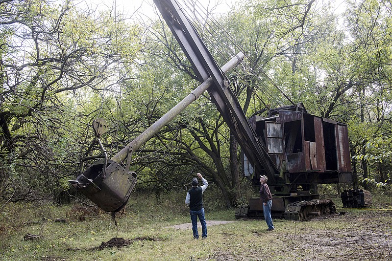 FILE--In this Oct. 16, 2018 file photo, Jim Lovell, left, and Carmen Boccia look over the Markley shovel where it has been for 70 years in nearby Cherokee, Kan. The historic coal mining shovel that was hidden under bramble for more than 70 years has gone on display in southeast Kansas alongside its more well-known successor, an 11 million pound orange giant known as Big Brutus. The Joplin Globe reports that a ceremony to dedicate the Markley shovel is slated for 1 p.m. Saturday at the Big Brutus Visitors Center, a nonprofit museum in West Mineral. Coal mine operator Perry Markley designed and built the shovel in the early 1900s using junkyard parts. The machine was one of the first mining shovels to be equipped with a round dipper stick that allowed the bucket to swivel. (Roger Nomer/The Joplin Globe via AP, File)