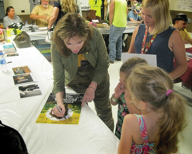 Pamula Pierce Barcelou, daughter of Charles B. Pierce who produced and directed the 1972 cult classic creature documentary "The Legend of Boggy Creek," signs movie posters for fans Saturday during the Fouke Monster Festival in Fouke, Ark. 