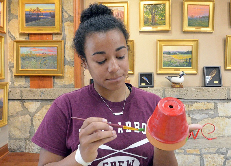 Jayla Anderson paints a message of encouragement on one of the flower pots that will be distributed to areas impacted by the tornado Tuesday at Capital Arts. Capital Arts invited individuals and groups to paint rocks and pots that will be distributed.
