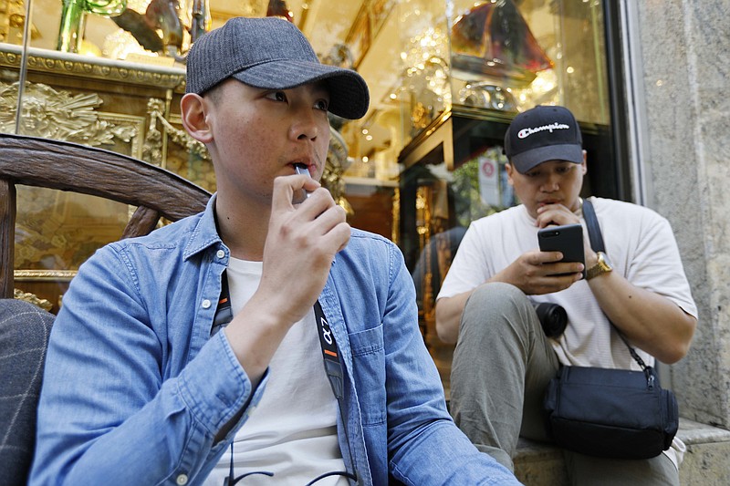 In this Monday, June 17, 2019, photo, Joshua Ni, 24, and Fritz Ramirez, 23, vape from electronic cigarettes in San Francisco. San Francisco supervisors are considering whether to move the city toward becoming the first in the United States to ban all sales of electronic cigarettes in an effort to crack down on youth vaping. The plan would ban the sale and distribution of e-cigarettes, as well as prohibit e-cigarette manufacturing on city property. (AP Photo/Samantha Maldonado)