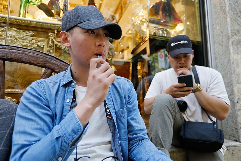 In this Monday, June 17, 2019, photo, Joshua Ni, 24, and Fritz Ramirez, 23, vape from electronic cigarettes in San Francisco. San Francisco supervisors are considering whether to move the city toward becoming the first in the United States to ban all sales of electronic cigarettes in an effort to crack down on youth vaping. The plan would ban the sale and distribution of e-cigarettes, as well as prohibit e-cigarette manufacturing on city property. (AP Photo/Samantha Maldonado)