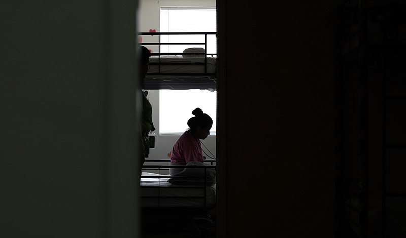 In this July 9, 2019, photo, an immigrant sits in her room at the U.S. government's newest holding center for migrant children in Carrizo Springs, Texas.  The government said the holding center will give it much-needed capacity to take in more children from the Border Patrol. (AP Photo/Eric Gay)