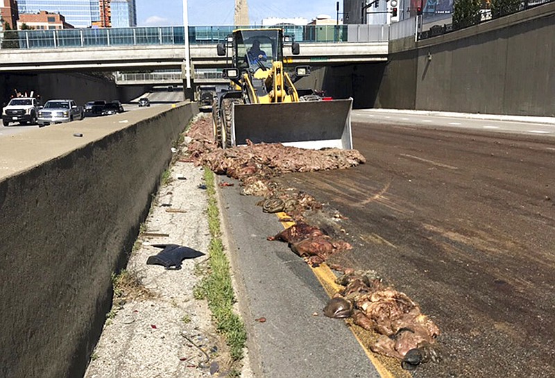 In this Thursday, July 11, 2019 photo, provided by the Missouri Department of Transportation, Kansas City District, a person operates a bulldozer as it cleans up after a tractor-trailer hauling pig intestine dumped its load across a downtown highway in Kansas City, Mo. (Missouri Department of Transportation, Kansas City District via AP)