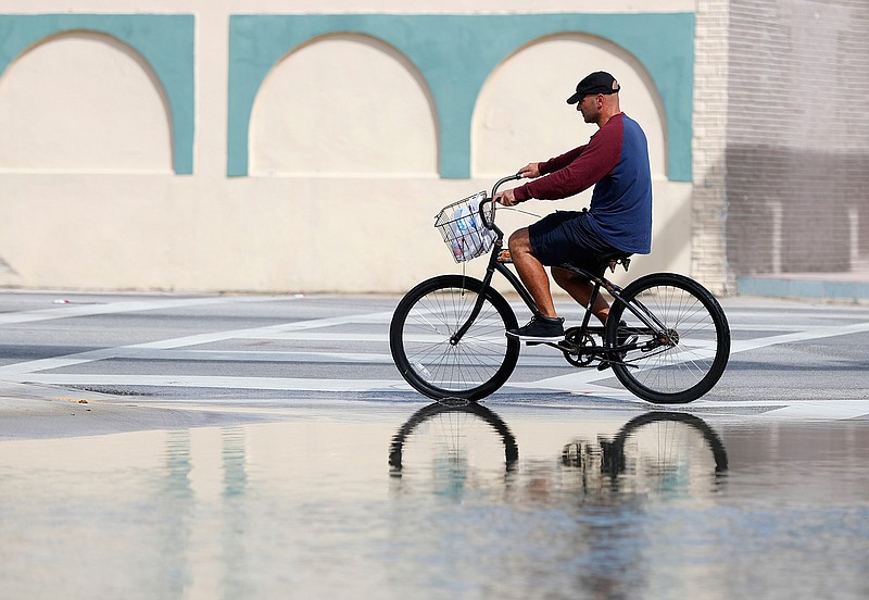 In this Oct. 9, 2018, file photo, a cyclist rides past an area flooded during a King Tide, an especially high tide, in Miami. Federal scientists, according to a report released Wednesday, July 10, 2019,  predict 40 places in the U.S. will experience higher than normal rates of so-called sunny day flooding this year due to rising sea levels and an abnormal El Nino weather system. (AP Photo/Wilfredo Lee, FIle)