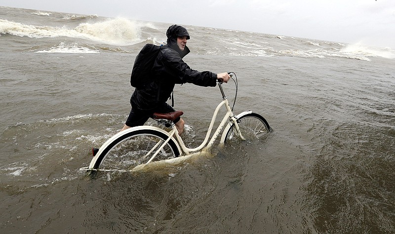 Tyler Holland guides his bike through the water as winds from Tropical Storm Barry push water from Lake Pontchartrain over the seawall Saturday, July 13, 2019, in Mandeville, La. (AP Photo/David J. Phillip)