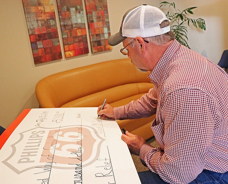 Deriek Gipson of Phillips 66 signs a check of $50,000 to the United Way of Central Missouri for disaster relief efforts at the United Way office Monday afternoon.