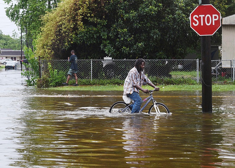 A man tries to bike through the flooding Sunday, April 24, 2019, after the rains of storm Barry on Louisiana Highway 675 in New Iberia, La. Tropical Depression Barry dumped rain as it slowly swept inland through Gulf Coast states Sunday. 