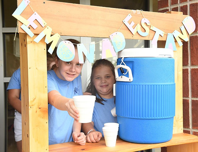 Olivia Carrender passes a cup of lemonade as her co-worker, Taylor Arlen, prepares to draw another glass of the liquid from the cooler. Students in Camp Jade at The Special Learning Center this week have done their part to help in tornado and flood recovery efforts by hosting a lemonade stand and bake sale. 
