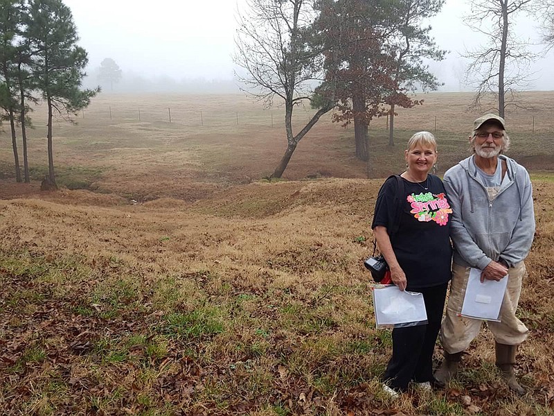 Brenda Mandella and Larry Collins are at the homes of their two families in Hughes Springs, Texas. Off to the left is a rut that is part of Trammel's Trace. The color of the grass changes, and the swale lips are visible passing off behind them to a creek. The trail would have taken off toward the top right of the photo but is lost because of cultivation.
(Photo by Gary Pinkerton)
