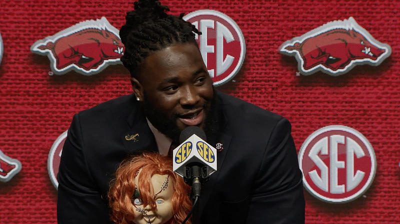 Arkansas defensive lineman McTelvin Agim holds a Chucky doll while speaking with reporters Wednesday during SEC Media Days in Hoover, Ala. The Texarkana native said the doll "represents my little cousin" John Neal Jr., who died in an unsolved homicide last year on the Texas side. (AP Photo/Butch Dill)

