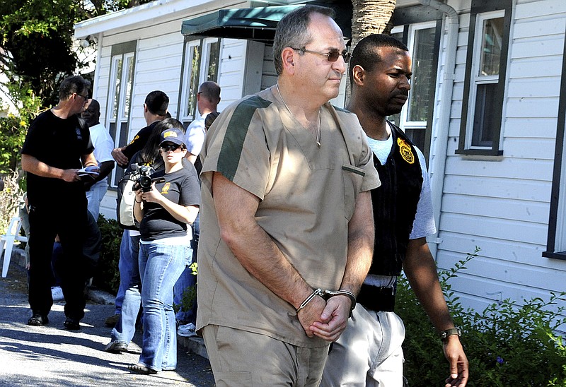 In this Feb. 2011 photo a DEA agent escorts Zvi Harry Perper to an awaiting police car after his Delray Pain Management clinic was raided by agents in Delray Beach, Fla.  Florida’s ‘pill mills’ were a gateway to the nation’s opioid crisis, feeding addiction and overdoses in Appalachia and other states. They exploded across Florida in the early 2000s and operated for years with little oversight. The release this week of July 19, 2019,  of a trove of federal data showing the distribution of opioids across the U.S. put the spotlight again on Florida’s notorious ‘pill mills,’ which provided the seeds of an epidemic that continues to cost tens of thousands of lives each year.  (Carline Jean/South Florida Sun-Sentinel via AP)