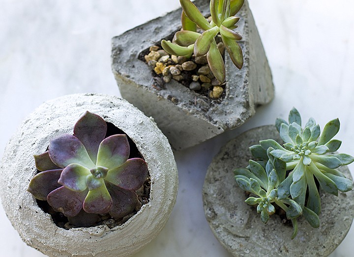 This July 7, 2019 photo shows small concrete planters in Strafford, N.H. Concrete planters can provide an industrial or rustic home for succulents and other small plants, and they're inexpensive and fairly easy to make. Spherical planters can be fashioned by applying cement to balloons, and bowls and other plastic containers can be used as molds for smoother results. A cardboard template taped together formed the mold for the more angular, geometric version shown here, top. (AP Photo/Holly Ramer)