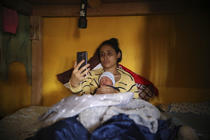 In this June 12, 2019 photo, Salvadoran teen migrant Milagro de Jesus Henriquez Ayala lies in bed with her newborn son Alexander, as she watches SpongeBob SquarePants on her smartphone, at the Agape World Mission shelter, in Tijuana, Mexico. Henriquez Ayala left middle school and has almost no job skills, and now she must find work that allows her to be with her baby, Alexander. (AP Photo/Emilio Espejel)