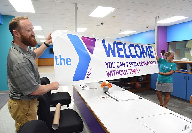 JULY 2019 FILE: Isaac Williams, near, and co-worker Angela Ramsey share a light-hearted moment as they unroll a new banner  preparing for the reopening of the Firley YMCA after it sustained extensive damage in the May 22 tornado. Williams is membership director and Ramsey is membership assistant. The Y reopens at 5 a.m. Aug. 1. 