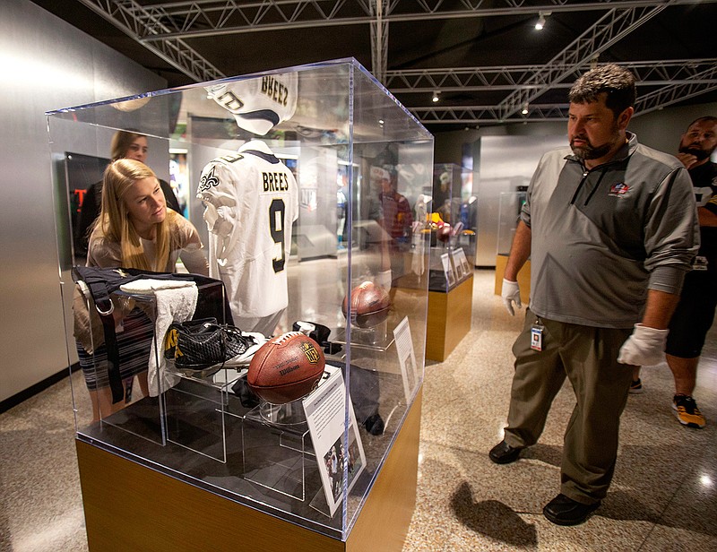 In this Oct. 9, 2018, file photo, Pro Football Hall of Fame curator Jason Aikens, right, watches Rachel Knapp as they work on a display in Canton, Ohio, of memorabilia of New Orleans Saints quarterback Drew Brees from his record-setting game against the Washington Redskins. Since opening in 1963 in Canton, Ohio, the hall just keeps growing, with a now 135,000-square foot building still not enough space to display all the jerseys, helmets, balls, gloves, Super Bowl rings and, of course, Hall of Fame busts. (Bob Rossiter/The Canton Repository via AP, File)
