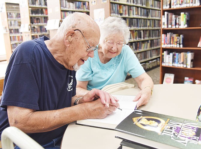 Ann Rackers assists her husband, David Rackers, on July 16, 2019, as he signs copies of the book "For Military Merit" at the Missouri River Regional Library. David is a Purple Heart Medal recipient for his service in the U.S. Army. 