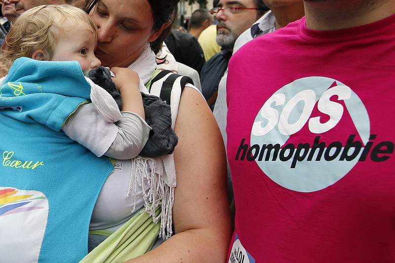 FILE - In this Saturday, June 28, 2014 file photo a woman kisses a baby next to a man wearing a shirt reading "SOS Homophobia" during the annual Gay Pride march in Paris, France. Single women and lesbians in France won't have to go abroad to have babies anymore under a proposed new law that would give them access to medically assisted reproduction for the first time. (AP Photo/Francois Mori, File)