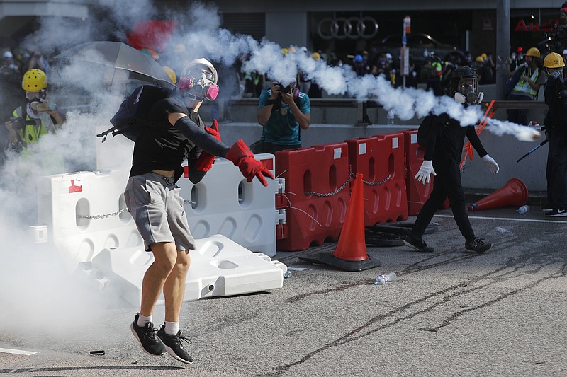 A protester throws back a tear gas canister in Hong Kong on Monday, Aug. 5, 2019. Droves of protesters filled public parks and squares in several Hong Kong districts on Monday in a general strike staged on a weekday to draw more attention to their demands that the semi-autonomous Chinese city's leader resign.(AP Photo/Vincent Thian)