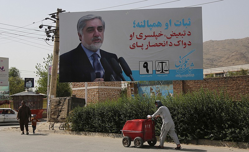 An Afghan ice-cream vendor walk past an election hoarding of a presidential candidate Abdullah Abdullah in Kabul,Afghanistan Friday, Aug. 9, 2019. Afghanistan faces a presidential election next month but few believe the vote will take place as the United States and the Taliban inch closer to a deal that could end the nearly 18-year war but bring uncertainty about almost everything else.  (AP Photo/Nishanuddin Khan)