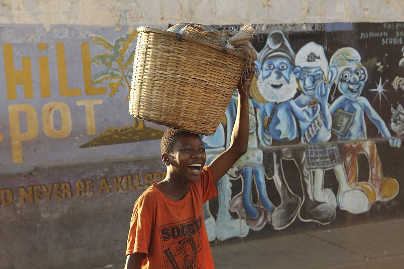 A young boy smiles while carrying a basket to a popular market in Harare, Thursday, Aug, 8, 2019. Many Zimbabweans who cheered the downfall of longtime leader Robert Mugabe two years ago have found the country's economy even worse than before.(AP Photo/Tsvangirayi Mukwazhi)