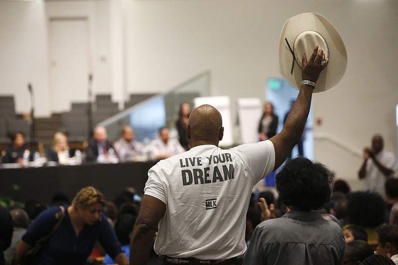 FILE - In this June 18, 2019 file photo a Phoenix resident stands up to wave his cowboy hat in support of a speaker at a community meeting in Phoenix. Still stinging from national outrage sparked this summer by a videotaped encounter of officers pointing guns and cursing at a black family, community members are holding low-key meetings aimed at helping Phoenix officials figure out how citizens could help oversee the city's officers. (AP Photo/Ross D. Franklin, File)