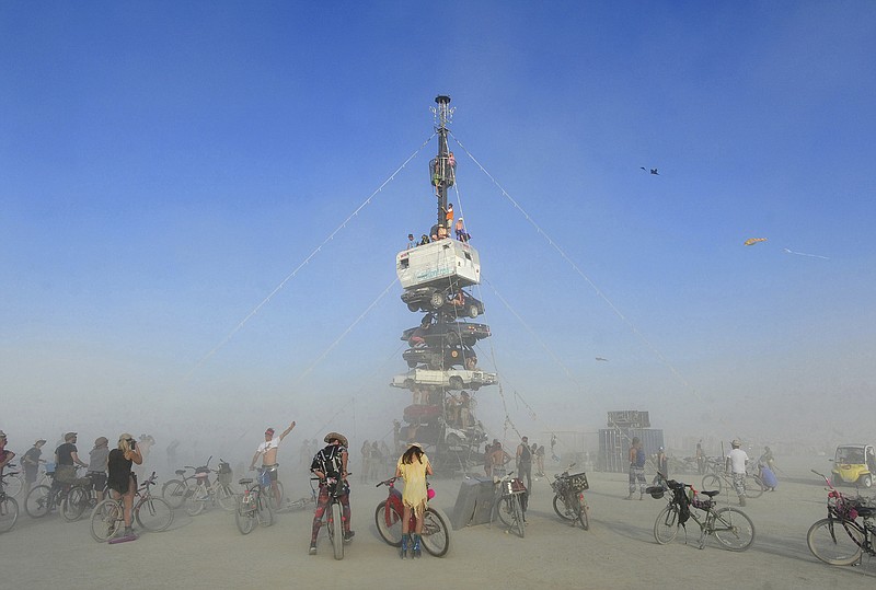 FILE -  this Monday, Aug. 27, 2018 file photo, burners surrounded by playa dust climb onto an art installation titled, "Night of the Climb," at Burning Man, in Gerlach, Nev. Experts say playa dust doesn't pose any significant health risk to those who inhale it during the annual counter-culture festival in the desert. (Andy Barron/The Reno Gazette-Journal via AP, File)