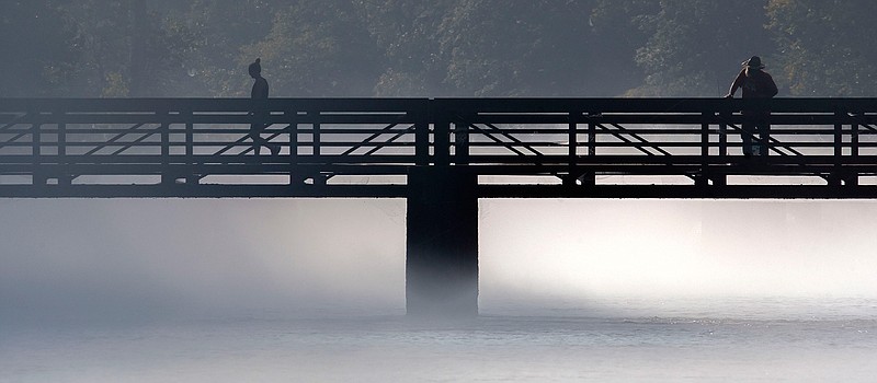 A woman walks across the bridge to Osceola Island just below the South Holston Lake dam in Sullivan County, Tennessee as a man fishes early Tuesday, August 20, 2019. (Andre Teauge/Bristol Herald Courier via AP)