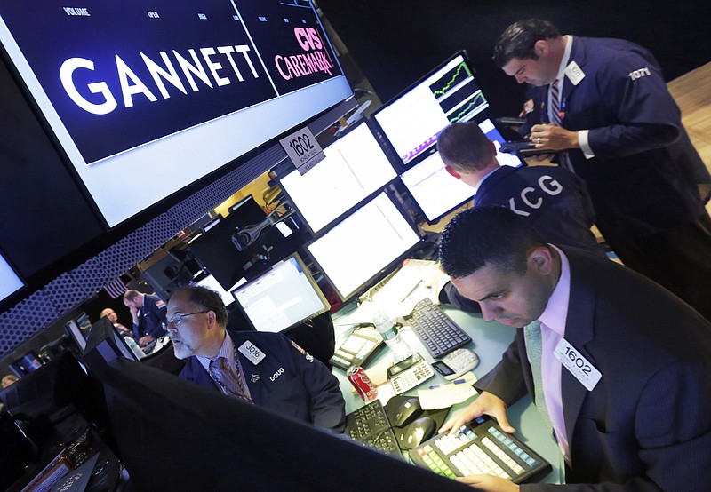 FILE - In this Aug. 5, 2014, file photo, specialist Michael Cacace, foreground right, works at the post that handles Gannett on the floor of the New York Stock Exchange. Just a week after announcing its $1.4 billion acquisition of Gannett, GateHouse Media is again laying off journalists and other workers at its newspapers, possibly foreshadowing the future awaiting employees of what will become the largest U.S. newspaper company. GateHouse and Gannett say the merger will allow GateHouse to accelerate the “digital transformation” of its newspapers while paying down huge sums GateHouse borrowed in order to fund the acquisition.  (AP Photo/Richard Drew, File)