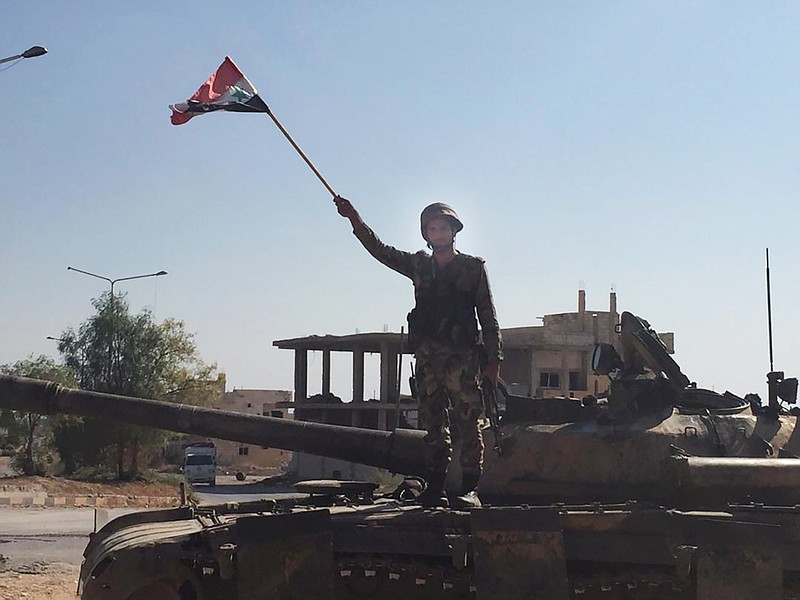 A Syrian soldier stands on a tank waving a national flag in the northwestern town of Khan Sheikhoun, Syria, on Saturday, Aug. 24, 2019.  The town was captured by Syrian troops this week after a monthslong offensive.  (AP Photo/Albert Aji)