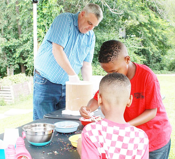 John Mollenkamp, a volunteer and husband to Common Ground Executive Director Tina Mollenkamp, helps serve ice cream to local community children, Jerry White, 9, and his little brother, Jayar White, 4, during Saturday's ice cream social at the Common Ground Community Building. 