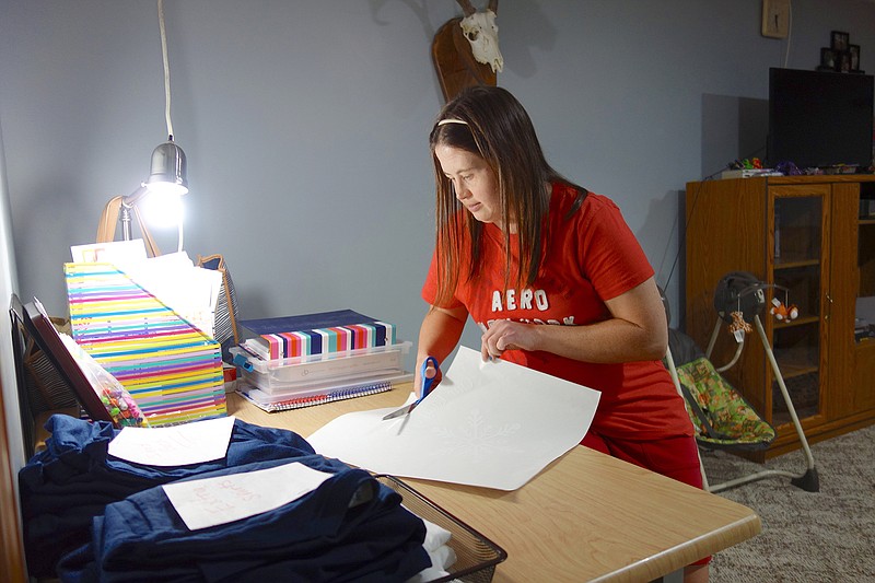 Stephanie Love cuts out the transfer designs and sorts different sizes of T-shirts so her mother, Tammy, can press the designs.