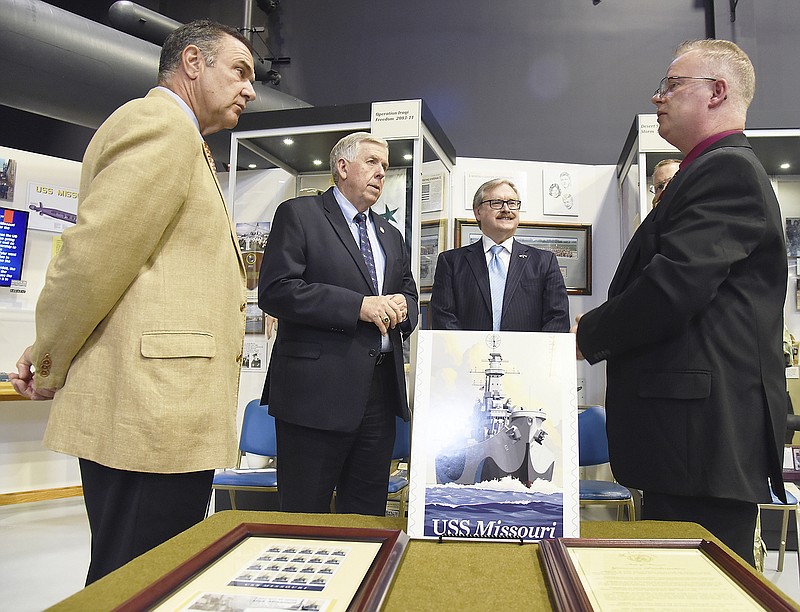 Museum of Missouri Military History Director Charles Machon, right, talks to visitors Lt. Gov. Mike Kehoe, left, Gov. Mike Parson, second from left, and Cole County Presiding Commissioner Sam Bushman immediately following a brief ceremony Tuesday during which Machon was presented with the framed sheet of stamps issued by the U.S. Postal Service and a gubernatorial proclamation, both shown in foreground. The event was held to celebrate the 75th anniversary of the commissioning of the battleship USS Missouri BB-63.