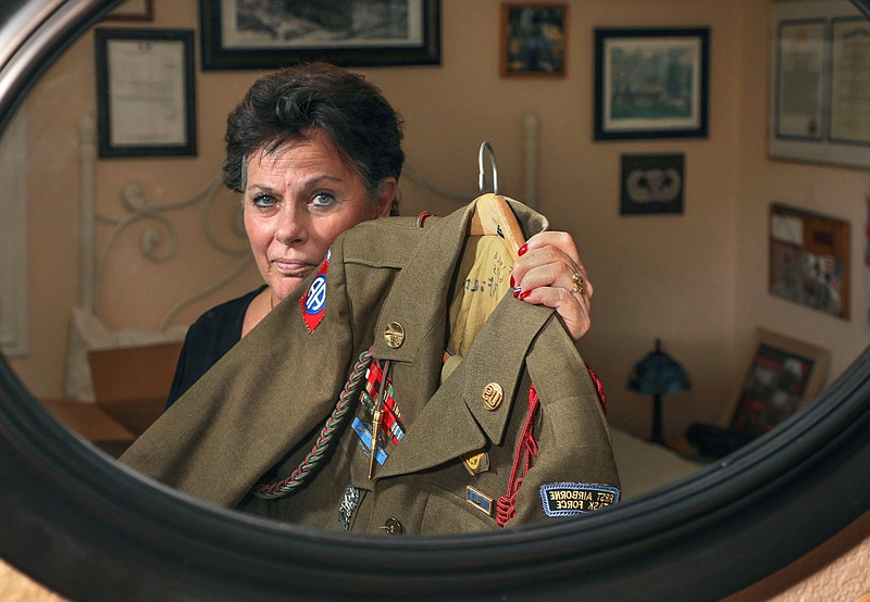 Portrait of Ginni Field, reflected in a mirror, holding the U.S. Army uniform of her late father Richard "Dick" Field. On the wall behind her are some of the many awards and honors from his combat experiences with the 551st Parachute Infantry Battalion in Operation Dragoon and the Battle of the Bulge, among others. (Charlie Neuman/The San Diego Union-Tribune/TNS) 