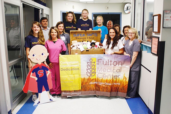 "Super" Sam's sister, Ava Santhuff, far left, and volunteers in navy blue shirts, Lexi Hux, Brooke Czschin and Adeline Nickelson, unveil the Super Sam Foundation's treasure chest at Fulton Medical Center with staff members. The treasure chest is to provide toys and other items to help put young patients or children in the waiting room at ease and overcome hospital stigmas.