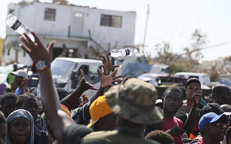 A Bahama's Army officer delivers water to people evacuated prior boarding a ferry to Nassau at the Port in Marsh Harbor, Abaco Island, Bahamas, Saturday, Sept. 7, 2019. The Bahamian health ministry said helicopters and boats are on the way to help people in affected areas, though officials warned of delays because of severe flooding and limited access.  (AP Photo/Fernando Llano)