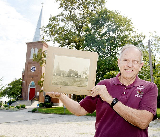 Pastor Gerald Scheperle holds an old photograph Monday showing the original church building, which still stands, and parsonage next door. He visited with a reporter and talked about the remodelings and changes made over the years at St. John's Lutheran Church in Schubert. The congregation will soon be celebrating the 150th anniversary of its organization.