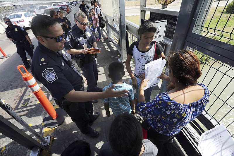 FILE - In this July 17, 2019, file photo, a United States Customs and Border Protection Officer checks the documents of migrants before being taken to apply for asylum in the United States, on International Bridge 1 in Nuevo Laredo, Mexico. A federal judge in California has reinstated a nationwide halt on the Trump administration's plan to prevent most migrants from seeking asylum on the U.S.-Mexico border. U.S. District Judge Jon Tigar on Monday, Sept. 9 ruled that an injunction blocking the administration's policy from taking effect should apply nationwide. (AP Photo/Marco Ugarte, File)