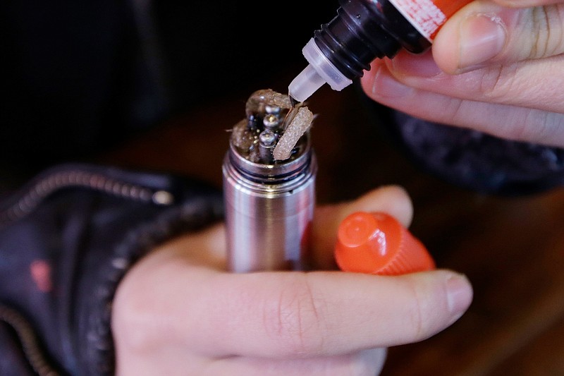 FILE - In this Feb. 20, 2014 file photo, a liquid nicotine solution is poured into a vaping device at a store in New York. In September 2019, U.S. health officials are investigating what might be causing hundreds of serious breathing illnesses in people who use e-cigarettes and other vaping devices. They have identified about 450 possible cases in 33 states, including six deaths. (AP Photo/Frank Franklin II)