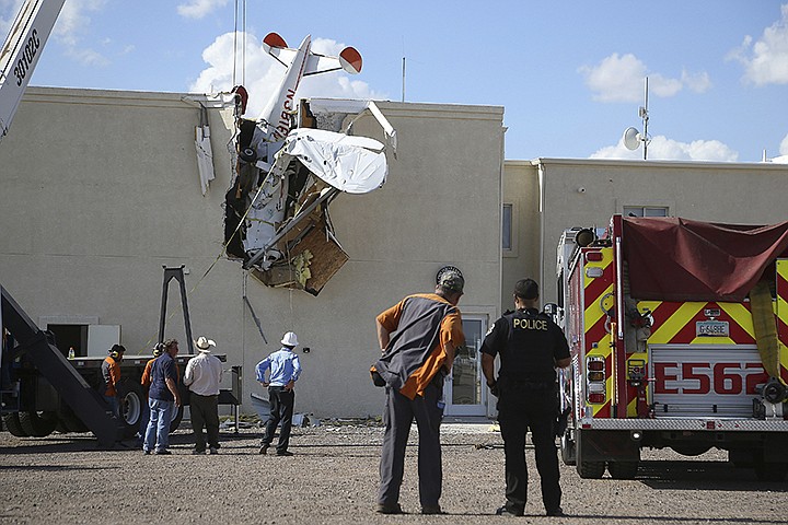Police and fire personnel look on as workers remove a single-engine plane after it crashed into the terminal building shortly after takeoff at the Ak-Chin Regional Airport Tuesday, Sept. 10, 2019, in Maricopa, Ariz. The two people onboard suffered non-life-threatening injuries. (AP Photo/Ross D. Franklin)
