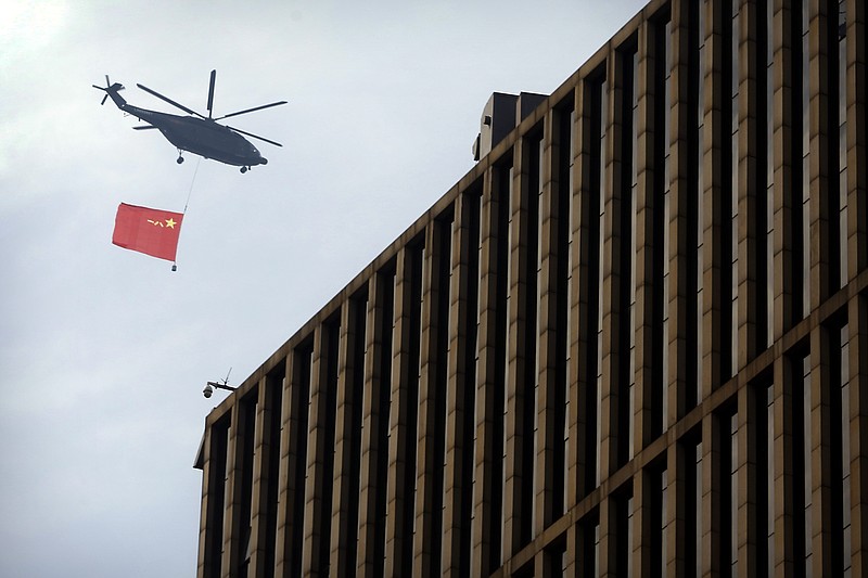 A helicopter carrying the flag of China's People's Liberation Army (PLA) flies above the central business district in Beijing, Sunday, Sept. 15, 2019. Many of the streets in the central part of China's capital were shut down this weekend for a rehearsal for what is expected to be a large military parade on Oct. 1 to commemorate the 70th anniversary of Communist China. (AP Photo/Mark Schiefelbein)