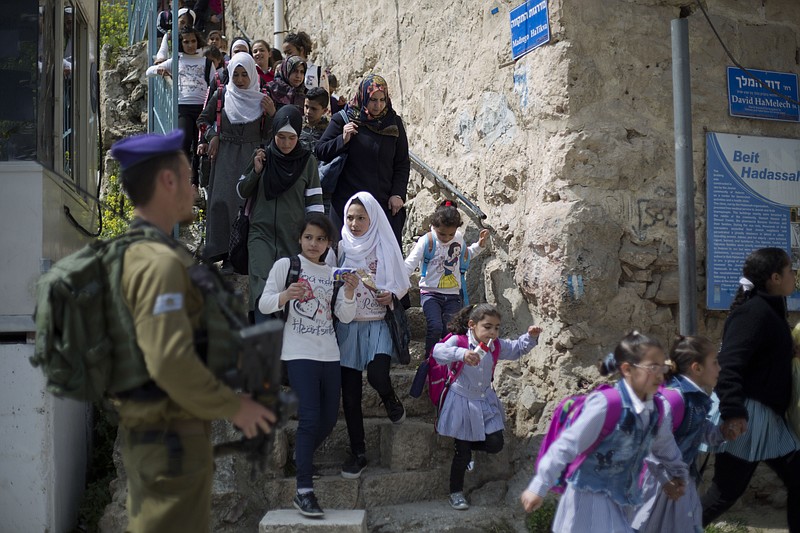 FILE - In this March 21, 2019 file photo, an Israeli solider stands guard as Palestinian school children cross back from school in the Israeli controlled part of the West Bank city of Hebron.  Israeli Prime Minister Benjamin Netanyahu vowed Monday Sept. 16, 2019, to annex "all the settlements" in the West Bank, including one in Hebron, an enclave deep in the heart of the largest Palestinian city, in a last-ditch move that appeared aimed at shoring up nationalist support the day before a do-over election. (AP Photo/Ariel Schalit, File)